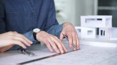 Planlar ve dizüstü bilgisayarlar üzerinde işbirliği yapan mimarlar, teknik çizimlere işaret ediyor ve bir bina projesi için çağdaş bir ofis toplantısında yapısal planlar ve tasarım ayrıntılarını tartışıyor