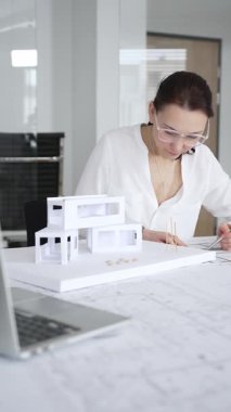 Kadın mimar, ayrıntılı bina planları üzerinde titizlikle çalışıyor. Masasına yayılmış. Mimari tasarımları parlak bir şekilde geliştirirken bir kalem ve cetvel kullanmak. Çağdaş ofis ortamı