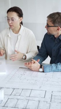 Mimarlar tasarım üzerinde işbirliği yapıyor, modern ofis ortamında planlar ve mimari modelleri tartışıyor, inşaat planlama ve mühendislik projelerinin geliştirilmesine odaklanıyor