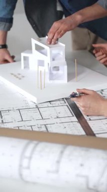 Mimarlar, tasarım ayrıntıları üzerinde işbirliği yaparak ve inşaat için yeni bir konut inşaatı projesi planlayarak, temiz bir masadaki planları ve ölçekli bir modeli inceleyecekler.