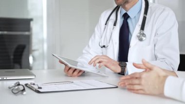 Doktorun hastaya danışması, bir klinik masasında tablet kullanması modern tıp ve dijital sağlık hizmetleri teşhisini sembolize ediyor. Tıp, sağlık ve bilim konsepti