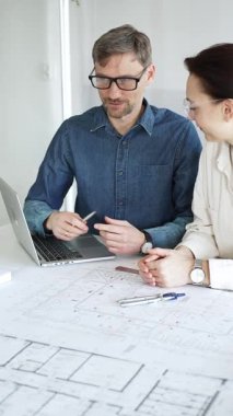 Mimarlar ve planlamacılar pusula ve dizüstü bilgisayarla ayrıntılı planları inceleyerek, bir konut projesinin kesin konut planlarını geliştirmek için bir ölçek modeli üzerinde işbirliği yapıyorlar