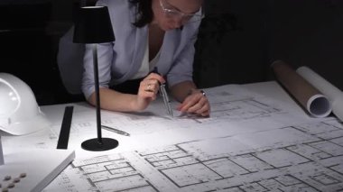 Mimar eller pusulayı kullanarak sabit şapkalı, lambalı ve yuvarlak planlı bir masanın planına kesin çizgiler çizer ve ölçer..