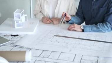 Mimarlar ve planlamacılar pusula ve dizüstü bilgisayarla ayrıntılı planları inceleyerek, bir konut projesinin kesin konut planlarını geliştirmek için bir ölçek modeli üzerinde işbirliği yapıyorlar