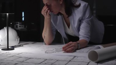 Stresli profesyonel kadın mimar ofiste gece geç saatlere kadar çalışıyor, bunalmış ve planlar yüzünden tükenmiş hissediyor. İş ve mimarlık kavramı