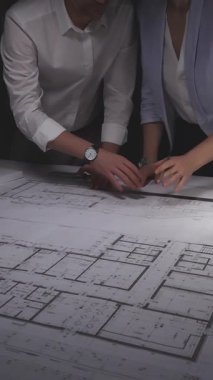 Profesyonel ekip bir masanın mimari planlarını inceliyor, tasarım detaylarını tartışıyor ve yeni bir inşaat projesi planlıyorlar. Gösterişsiz ışıklandırmada mimari ve iş kavramı