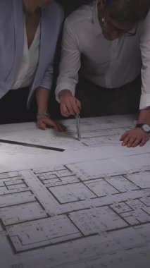 Detaylı mimari planları ve kat planlarını inceleyen iki profesyonel, yeni bir bina tasarımı projesi için ölçümler yapıyor. Gösterişsiz ışıklandırmada mimari ve iş kavramı