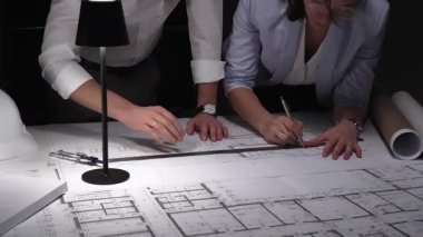 Mimarlar birlikte çalışır, bina planlarını ve planlarını analiz eder, bir ofiste tasarım kavramlarını ve mühendislik unsurlarını tartışırlar..