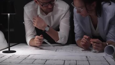 Mimarlar birlikte çalışır, bina planlarını ve planlarını analiz eder, bir ofiste tasarım kavramlarını ve mühendislik unsurlarını tartışırlar..