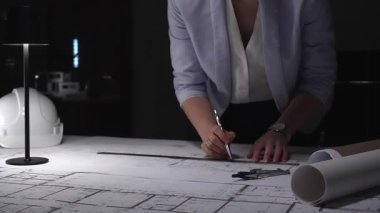 Profesyonel mimar mimari planlar tasarlıyor, masa lambasının altına çizgiler çiziyor, hassasiyet ve adanmışlığı vurguluyor