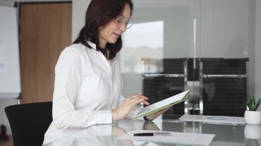 Modern cam bir masada dijital tabletle çalışan profesyonel bir ortamda çalışan kadın, üretkenliği, yeniliği ve teknolojinin kurumsal ofis ortamında entegrasyonunu vurguluyor.