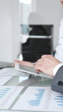 İş adamları kağıt grafikler ve dijital tabletler üzerindeki mali verileri analiz ediyor, pazar eğilimlerini gözden geçirmek ve modern ofis ortamında yeni stratejiler geliştirmek için işbirliği yapıyorlar