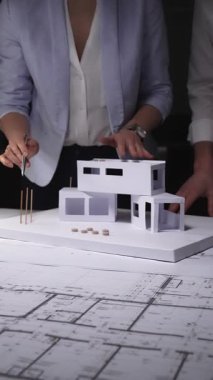 Mimarlar konut inşaatı tasarlar, ofis masasında kağıt modelli planlar analiz ederler, inşaat projesini geliştirirler. Mimarlık ve iş kavramı gösterişsiz ışıklandırmada