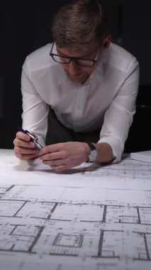 Mimari planlar üzerinde geç saatlere kadar çalışan mühendis, inşaatın detaylarını ölçmek ve çizmek için bir pusula kullanıyor. Gösterişsiz ışıklandırmada mimari ve iş kavramı