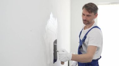 Profesyonel erkek inşaat işçisi, ev yenileme ve iç dekorasyon konusunda uzmanlığını göstermek için duvara alçı yapıştırmak için son bir mala kullanıyor. Dikey görünüm.