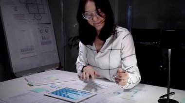 Finans raporlarını ve dijital tableti inceleyen iş kadını, strateji planlarken ve hedeflere ulaşmak için fazla mesai yaparken, veriler, çizelgeler ve belgelere odaklandı