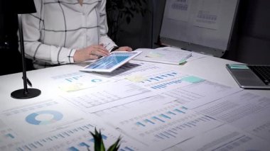 Piyasa analizi ve iş stratejisini optimize eden sayısız yazılı belge ile çevrili, finansal tablolar ve grafikler gösteren dijital tablet ekranına tıklayan iş profesyonelleri