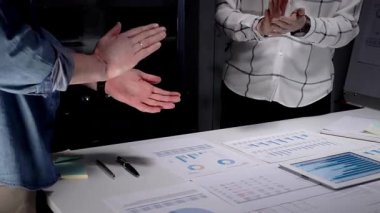 İş arkadaşları, mali belgeler, çizelgeler, tablet ve lambayla kaplı ofis masasını alkışlayarak, gece yarısı yapılan analizlerden sonra anlaşmaya işaret ediyor ve başarılı sonuçları kutluyorlar.