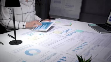 Piyasa analizi ve iş stratejisini optimize eden sayısız yazılı belge ile çevrili, finansal tablolar ve grafikler gösteren dijital tablet ekranına tıklayan iş profesyonelleri