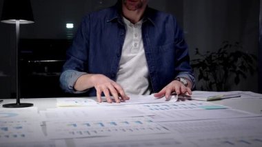 Geç saatlere kadar çalışan, ofis masasındaki dizüstü bilgisayardaki mali verileri ve iş raporlarını analiz eden, performans grafiklerini inceleyen ve planlama stratejisini lamba ışığında inceleyen, kurumsal büyümeyi yönlendiren bir adam.