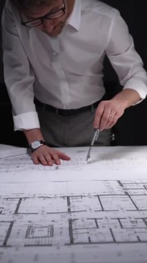 Adam mimari planlara odaklanıyor, yeni bir proje çözümü için kesin ölçümler hazırlıyor. Gösterişsiz ışıklandırmada mimari ve iş kavramı