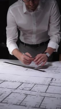 Profesyonel mimar veya mühendis bina tasarımını geliştiriyor, kat planları ve bir masanın üzerinde ölçeklendirilmiş mimari modelle çalışıyor. Gösterişsiz ışıklandırmada mimari ve iş kavramı