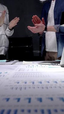 İş arkadaşları, mali belgeler, çizelgeler, tablet ve lambayla kaplı ofis masasını alkışlayarak, gece yarısı yapılan analizlerden sonra anlaşmaya işaret ediyor ve başarılı sonuçları kutluyorlar.