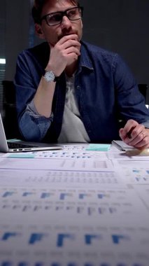 Gece geç saatlere kadar çalışan bir işadamı, mali verileri düşünüp analiz ediyor, ofis masasında doküman ve grafiklerle fazla mesai yapıyor, kendini başarıya adamış.