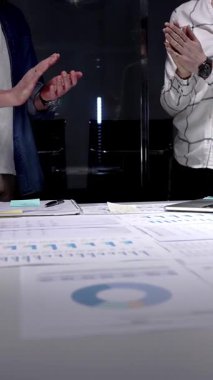 İş arkadaşları, mali belgeler, çizelgeler, tablet ve lambayla kaplı ofis masasını alkışlayarak, gece yarısı yapılan analizlerden sonra anlaşmaya işaret ediyor ve başarılı sonuçları kutluyorlar.