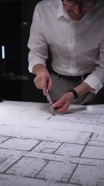 Adam mimari planlara odaklanıyor, yeni bir proje çözümü için kesin ölçümler hazırlıyor. Gösterişsiz ışıklandırmada mimari ve iş kavramı