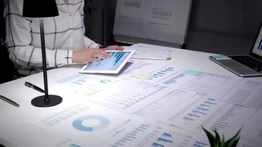 Piyasa analizi ve iş stratejisini optimize eden sayısız yazılı belge ile çevrili, finansal tablolar ve grafikler gösteren dijital tablet ekranına tıklayan iş profesyonelleri