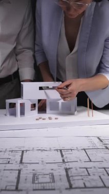 Mimarlar konut inşaatı tasarlar, ofis masasında kağıt modelli planlar analiz ederler, inşaat projesini geliştirirler. Mimarlık ve iş kavramı gösterişsiz ışıklandırmada