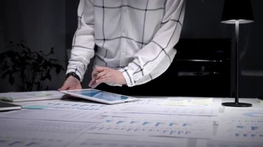 İşadamı karanlık bir ofisteki bir masaya odaklanmış, dizüstü bilgisayardaki mali raporları ve çizelgeleri analiz ediyor, gece yarısı üretkenlik oturumunda iş akışını yönetiyor.