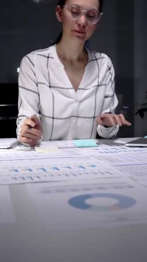 Profesyonel iş kadını elinde kalemle mali raporları analiz ediyor, iş belgeleri ve veri analizleri üzerinde geç saatlere kadar çalışıyor, şirket performansını artırmaya ve büyüme hedeflerine ulaşmaya odaklanıyor.
