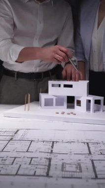 Mimarlar bir inşaat projesinde işbirliği yapıyor, mimari bir ev modeli ile çalışıyor ve bir masanın üzerinde bina planları hazırlıyor. Gösterişsiz ışıklandırmada mimari ve iş kavramı