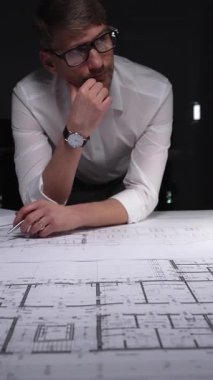 Mühendis ya da mimar, karmaşık bir inşaat projesi üzerinde çalışarak ayrıntılı bina planları ve planlarına yoğunlaşıyor. Gösterişsiz ışıklandırmada mimari ve iş kavramı