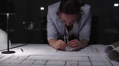 Gece geç saatlerde bir lambanın altındaki bir masanın mimari planlarını hazırlayan kadın mühendis. İş ve mimarlık kavramı