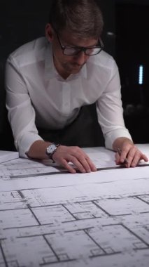 Mimari tasarımlar üzerinde çalışan erkek mimar, büyük kağıt kağıtlara dikkatlice ölçüyor ve kat planlarını çiziyor. Gösterişsiz ışıklandırmada mimari ve iş kavramı
