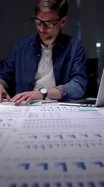 Gece geç saatlere kadar karanlık bir ofiste çalışan meşgul bir adam, stratejik planlama ve fazla mesai üretkenliği için dijital tablet kullanan finansal veriler, piyasa analizleri ve iş raporları üzerinde yoğunlaşıyor.