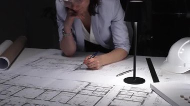 İşteki bıkkınlık ve yorgunluğu ifade eden, loş ofisteki mimari planları gözden geçiren profesyonellerin şaşkına dönmüş. İş ve mimarlık kavramı