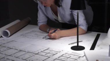 Mimar eller pusulayı kullanarak sabit şapkalı, lambalı ve yuvarlak planlı bir masanın planına kesin çizgiler çizer ve ölçer..