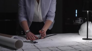 Profesyonel mimar mimari planlar tasarlıyor, masa lambasının altına çizgiler çiziyor, hassasiyet ve adanmışlığı vurguluyor