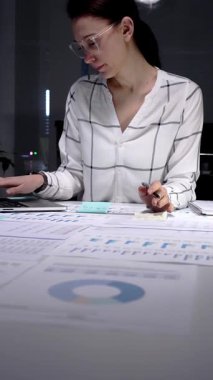 Profesyonel iş kadını elinde kalemle mali raporları analiz ediyor, iş belgeleri ve veri analizleri üzerinde geç saatlere kadar çalışıyor, şirket performansını artırmaya ve büyüme hedeflerine ulaşmaya odaklanıyor.