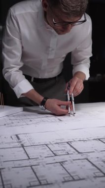 Adam mimari planlara odaklanıyor, yeni bir proje çözümü için kesin ölçümler hazırlıyor. Gösterişsiz ışıklandırmada mimari ve iş kavramı