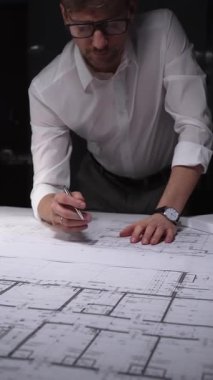 Mühendis ya da mimar, karmaşık bir inşaat projesi üzerinde çalışarak ayrıntılı bina planları ve planlarına yoğunlaşıyor. Gösterişsiz ışıklandırmada mimari ve iş kavramı