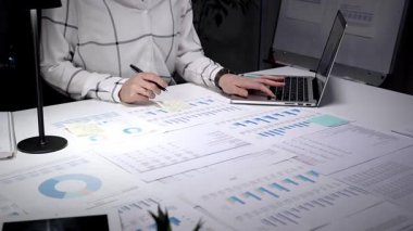 Geceleri titizlikle çalışan, sayısız basılı çizelge, grafik ve dizüstü bilgisayarla çevrili, henüz düzenlenmemiş bir masanın mali verilerini ve iş raporlarını titizlikle analiz eden bir kişi.