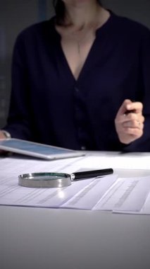 Tablet verilerini analiz eden ve loş bir ofis lambasının altındaki masada evrakları imzalayan bir kadın, gece geç saatlerde raporlara ve sözleşmelere odaklandı. İş dünyasında denetim ve vergi teması