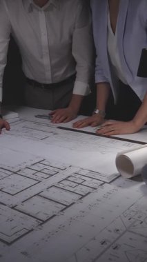Profesyonel ekip bir masanın mimari planlarını inceliyor, tasarım detaylarını tartışıyor ve yeni bir inşaat projesi planlıyorlar. Gösterişsiz ışıklandırmada mimari ve iş kavramı