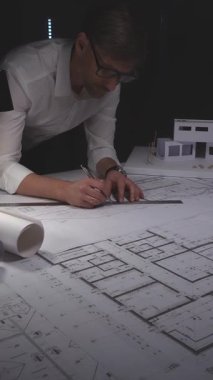 Mimar, bina planları, bir bina modeli ve mimari ve mühendislik planları ile ilgili ayrıntıları çiziyor. Gösterişsiz ışıklandırmada mimari ve iş kavramı