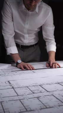 Profesyonel mimar veya mühendis bina tasarımını geliştiriyor, kat planları ve bir masanın üzerinde ölçeklendirilmiş mimari modelle çalışıyor. Gösterişsiz ışıklandırmada mimari ve iş kavramı